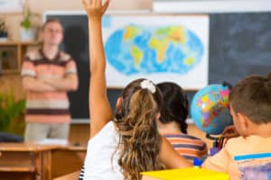 Young girl in classrom raising her hand. A Brief History of Accessibility Law in the U.S. ; accessibility laws