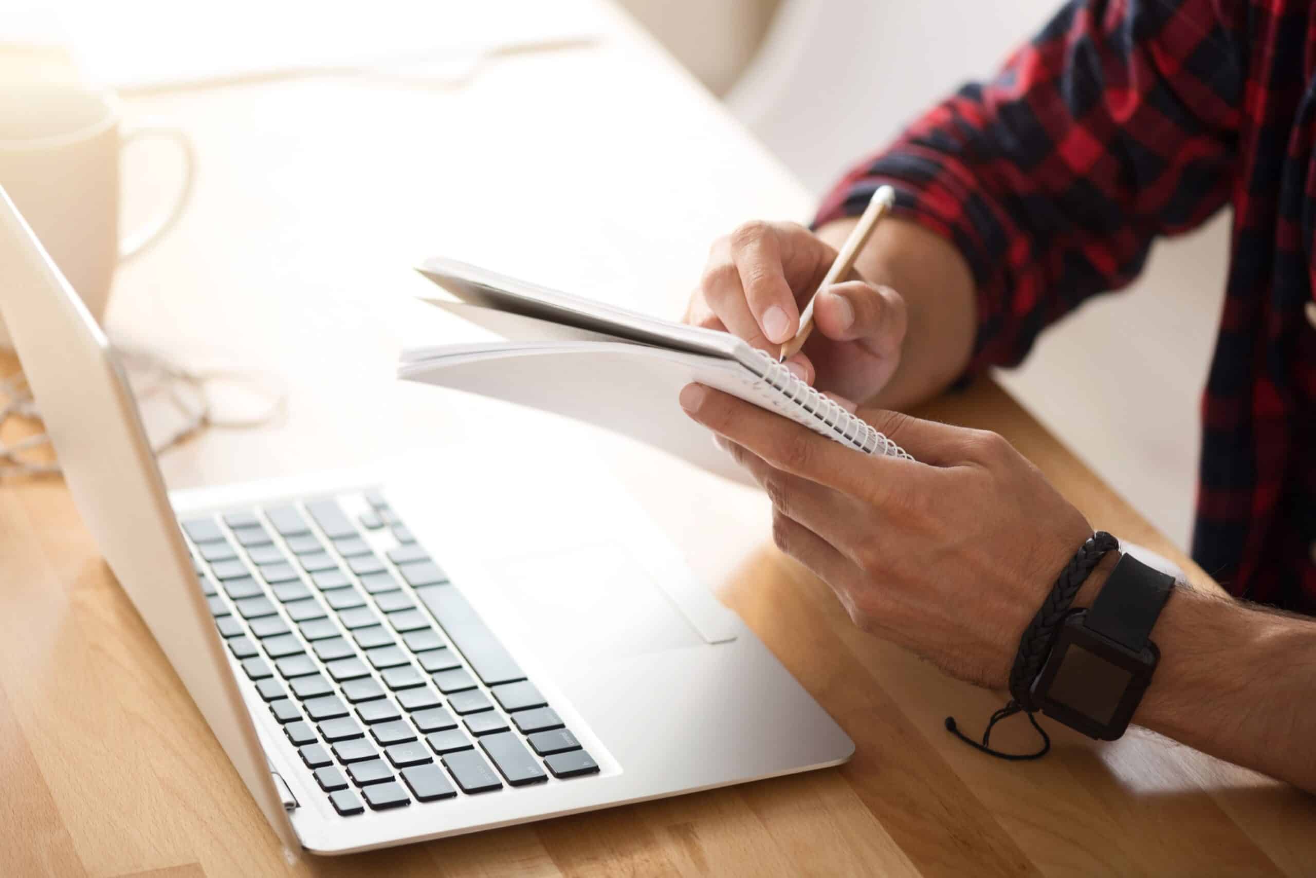 Man Sitting At The Table And Making Notes While Using Laptop. Accessibility Checkers