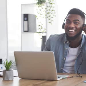 Smiling African American young man student in headphones watching video using audio description in classroom online