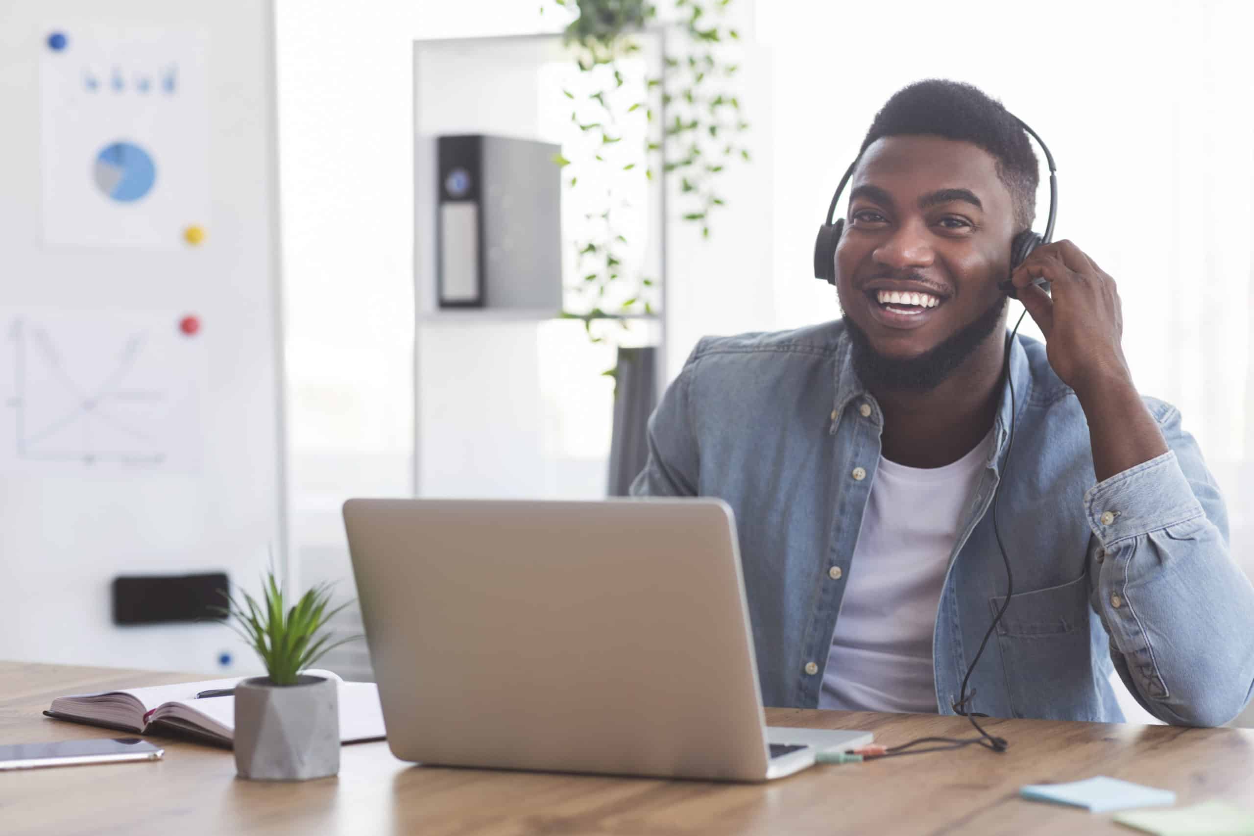 Smiling African American young man student in headphones watching video using audio description in classroom online