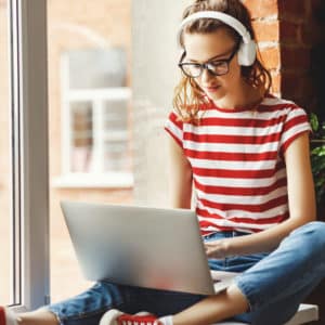 Calm young woman in headphones listening to music and working on laptop at home