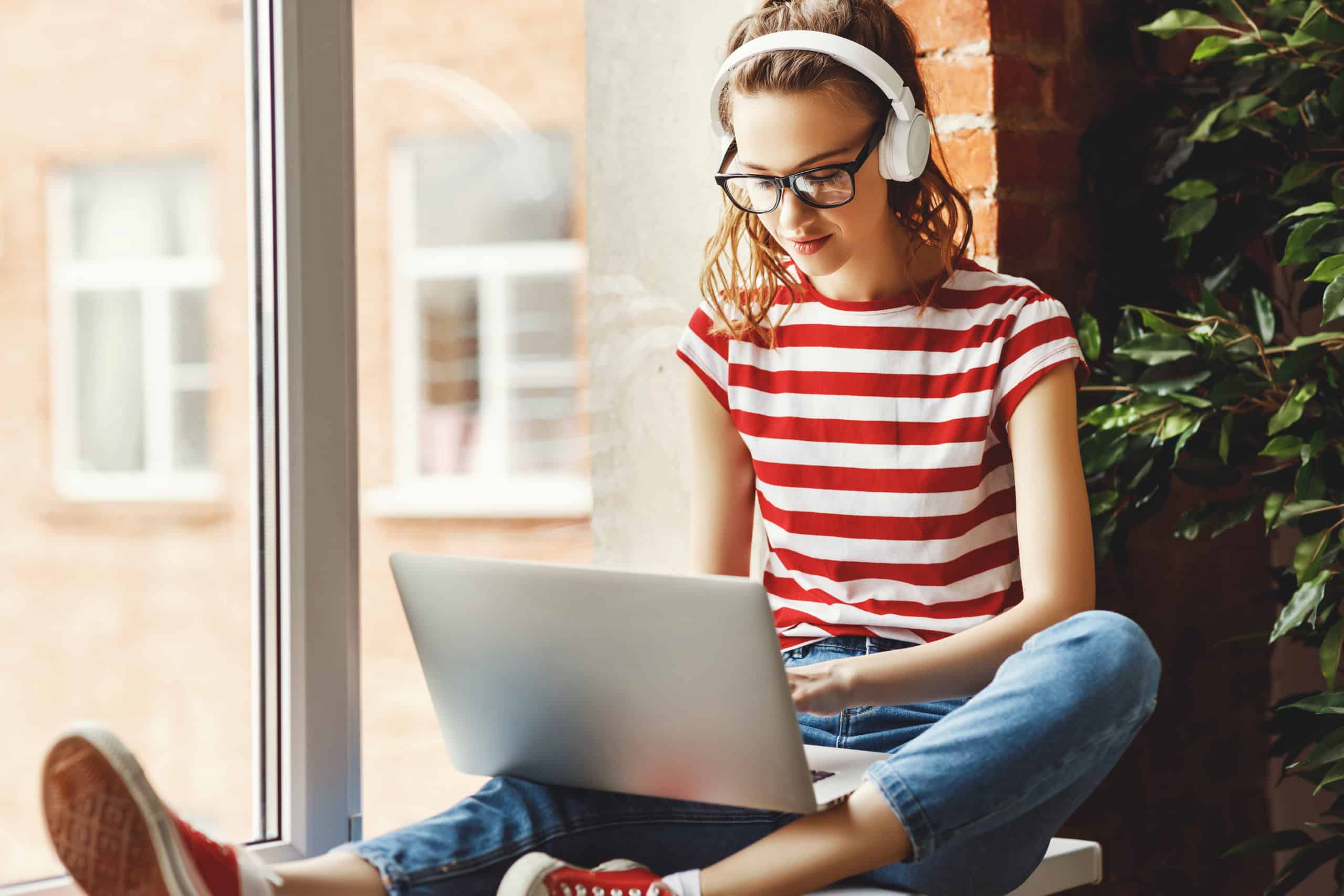 Calm young woman in headphones listening to music and working on laptop at home