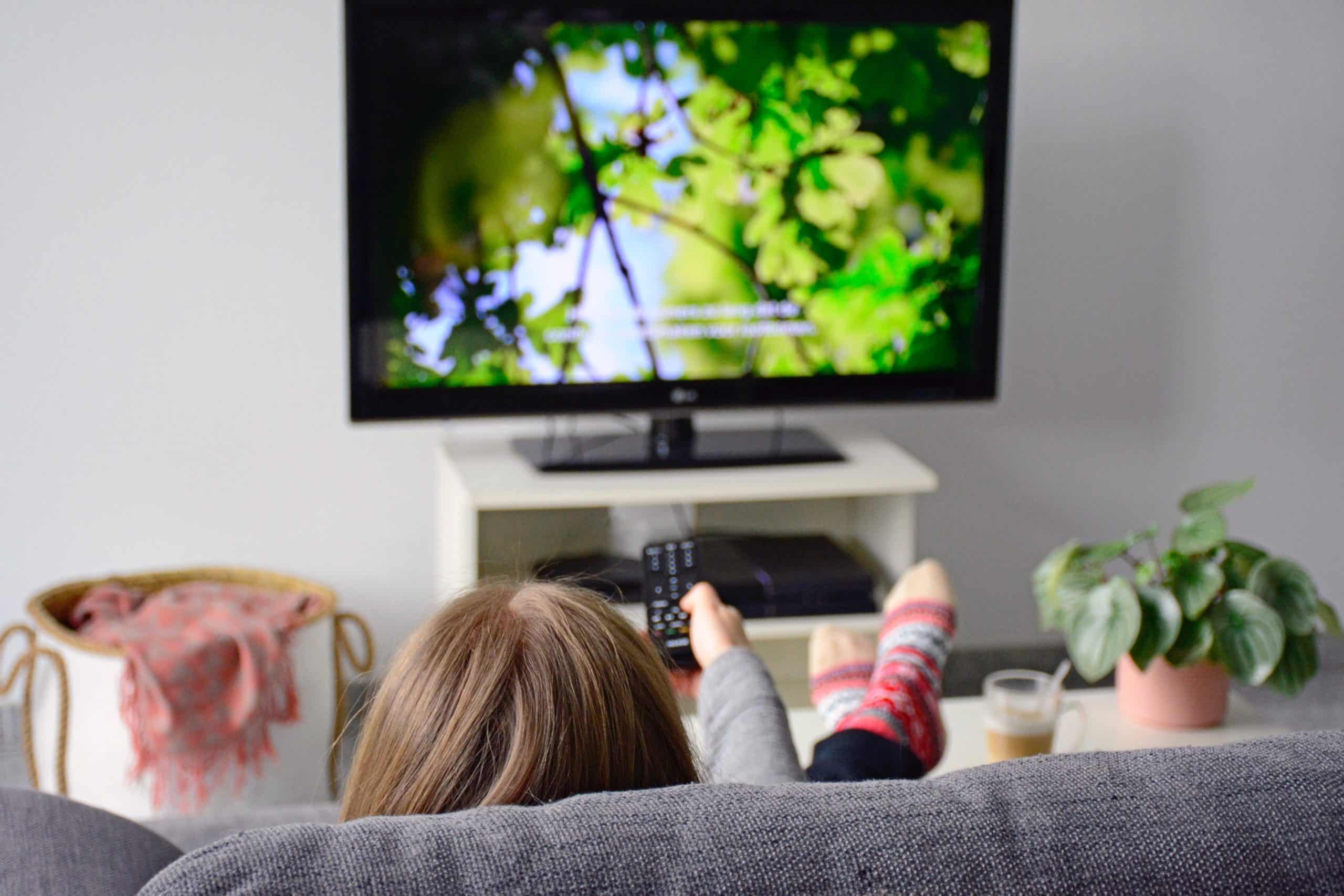 A young woman from behind watching TV while sitting on sofa in living room