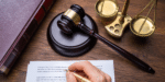 Person writing on paper with a gavel and scale.